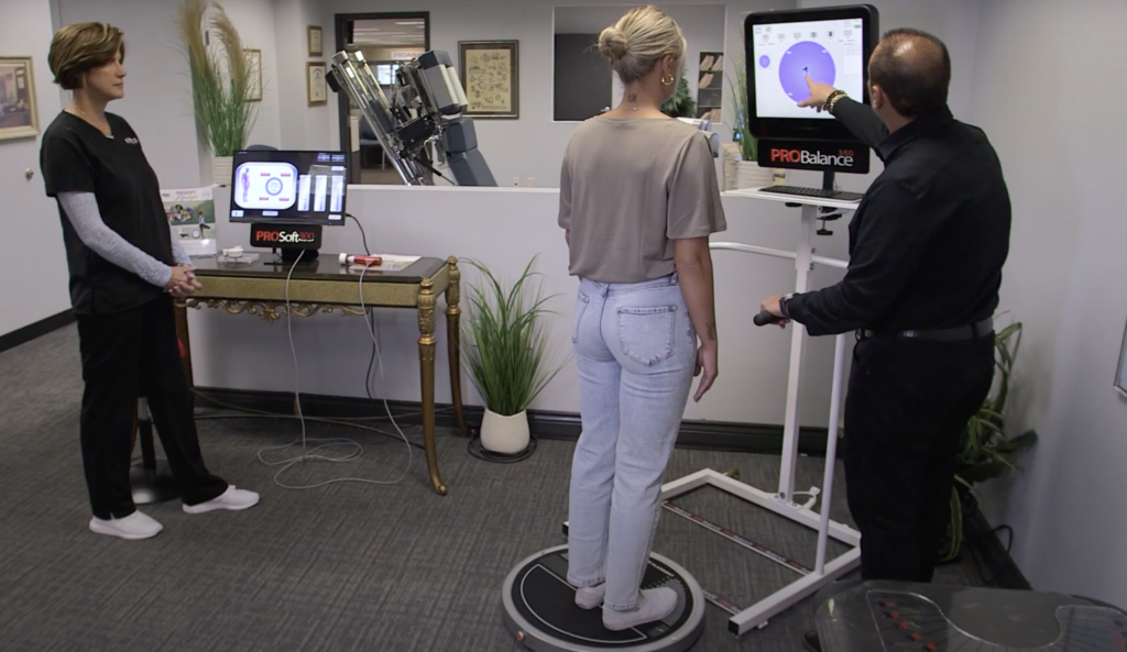 A chiropractor using the ProBalance device on a young woman while his chiropractic assistant stands by to assist if necessary.  
