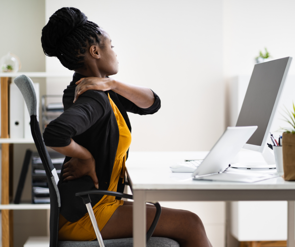 A woman holds her shoulder and back while sitting at her computer desk. 