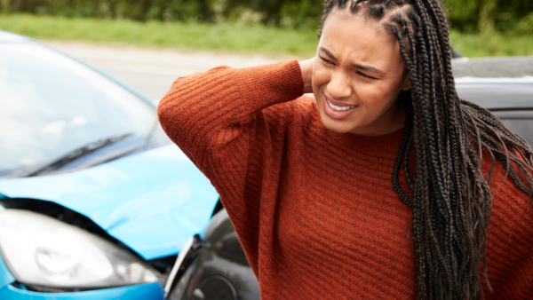 Woman holding her neck in front of two cars that crashed into each other. 